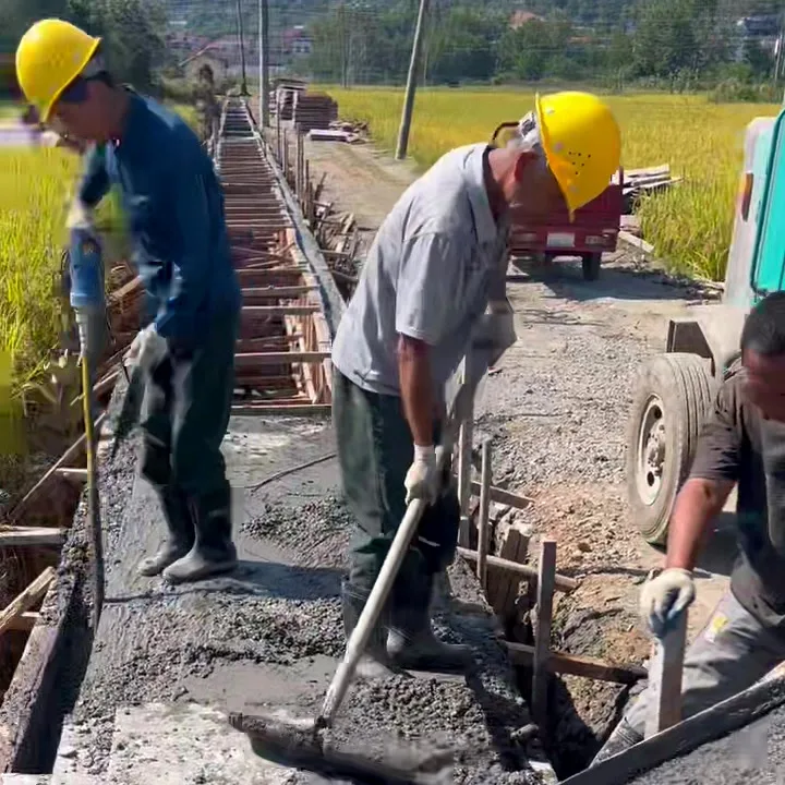 Three men finishing a narrow road pour beside a self-loading mixer on a rural site