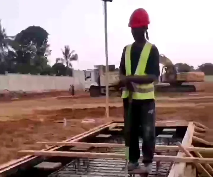 Worker in a hard hat and hi-vis vest standing on tied reinforcement in timber formwork, excavator and tipper behind