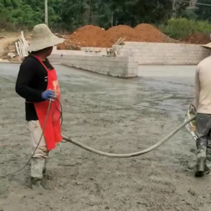 Two workers running poker vibrators across a freshly poured concrete slab on a rural site