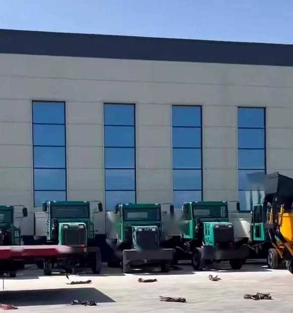 A row of cabs and chassis parked in a plant yard in front of a large assembly building